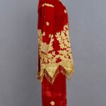 Strój ślubny uszyty z czerwonego materiału ze złotymi zdobieniami widziany od boku.